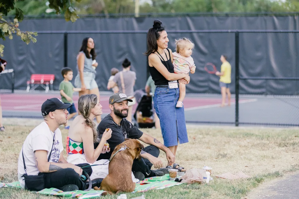 Festivalgoers relaxing on a picnic blanket with a dog beside the courts.