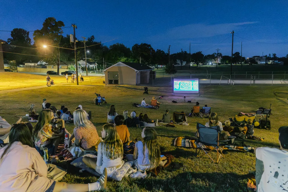 Neighbors watching the outdoor movie together as evening falls.