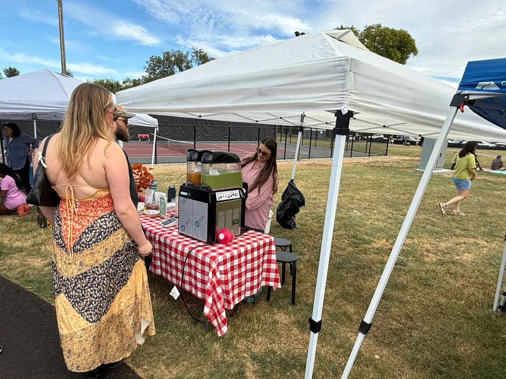 A festivalgoer visiting a coffee stand with a red checked tablecloth.